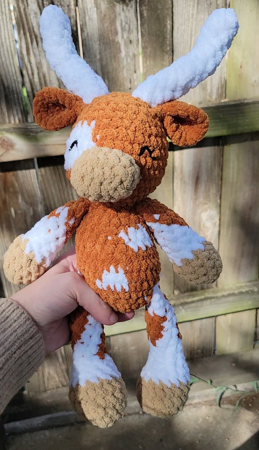 Hand holding a crocheted longhorn cow toy against a wooden background