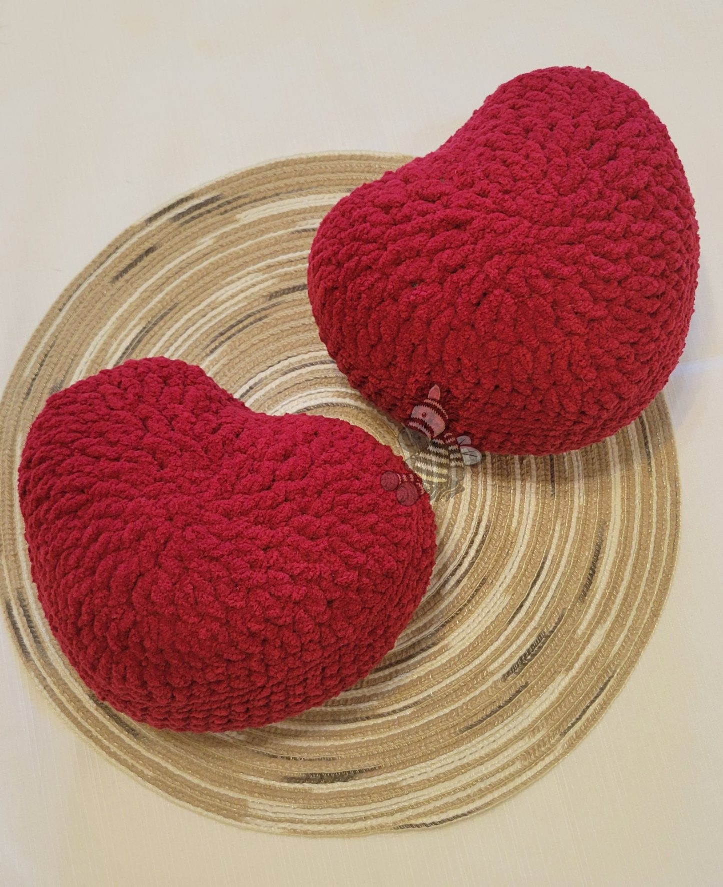 2 red crochet heart pillows on a wood grain circle with a white background