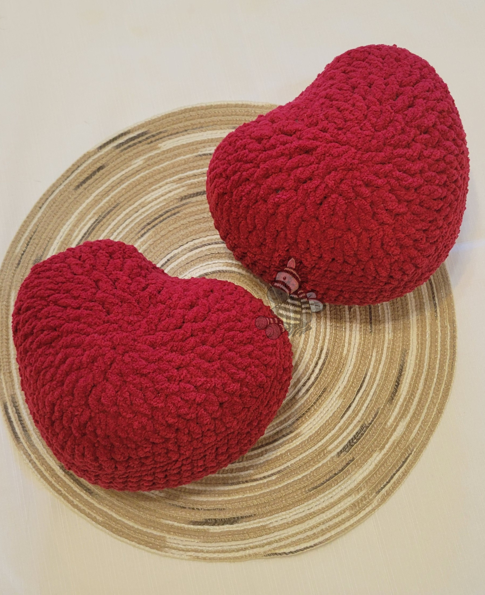 2 red crochet heart pillows on a wood grain circle with a white background