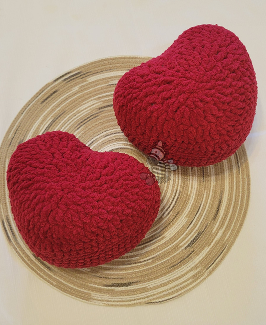 2 red crochet heart pillows on a wood grain circle with a white background