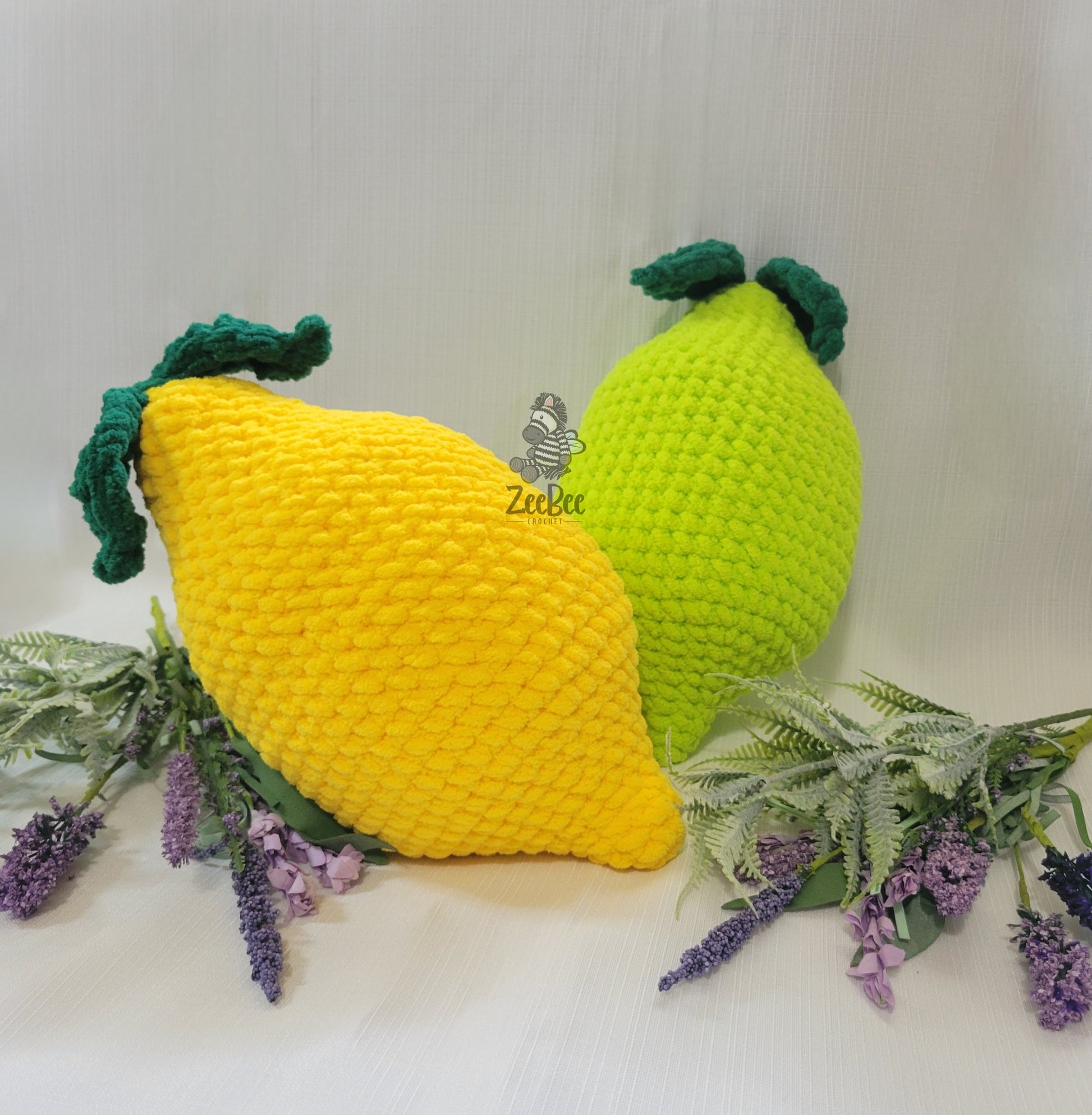 Crocheted lemon and lime pillows with green leaves on a white background