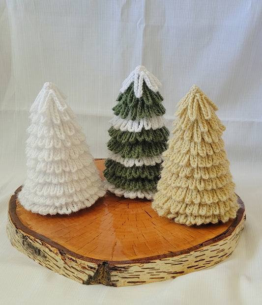 Three crocheted Christmas trees on a wooden base against a white background . colors are tan, white and green and white