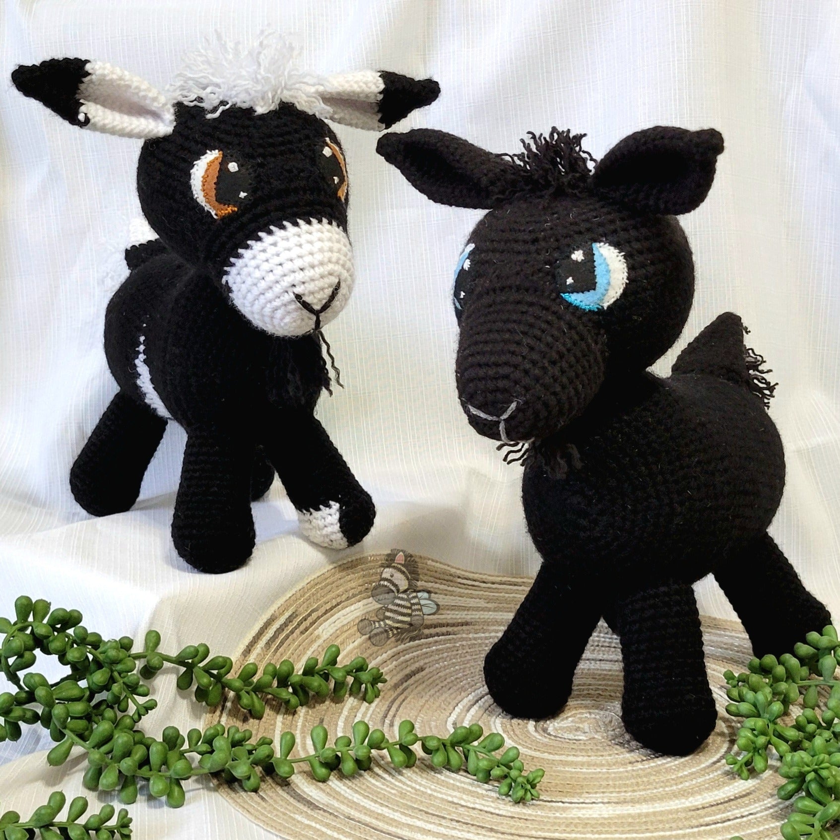 Two black crochet goats, one with white accents on a light background