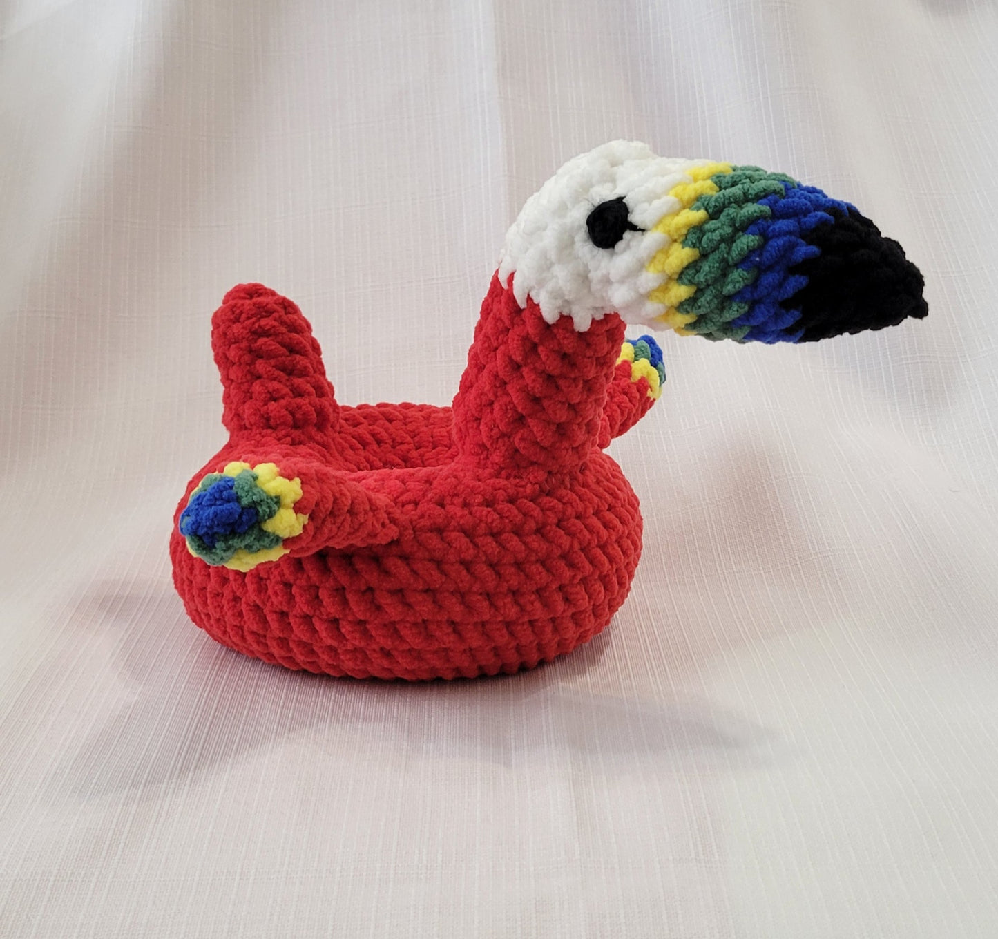 Crocheted parrot stuffed pool floatie toy with colorful beak on a light background