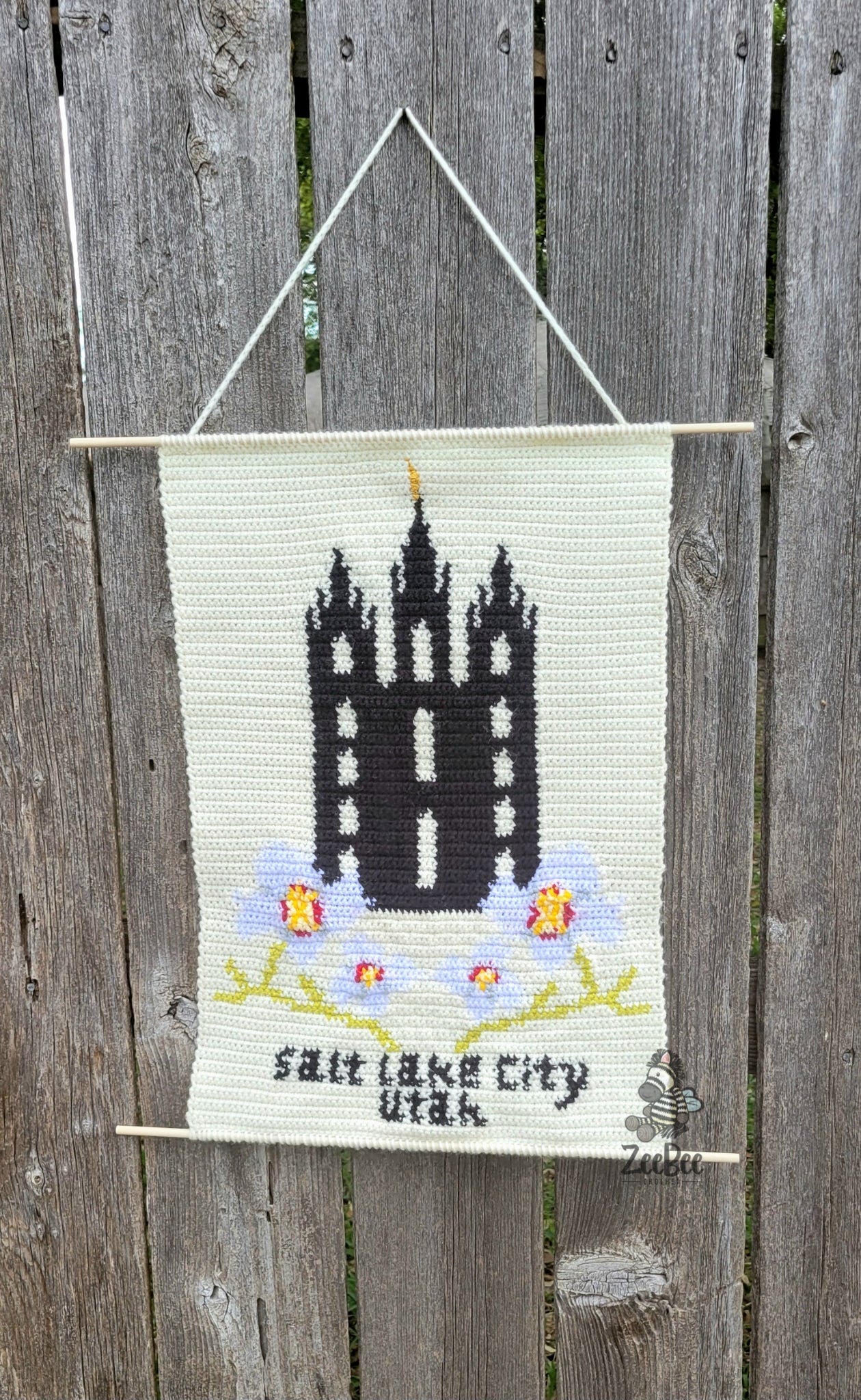 crocheted wall hanging with lds temple design and 'Salt Lake City, Utah' text, hanging on a wooden fence.