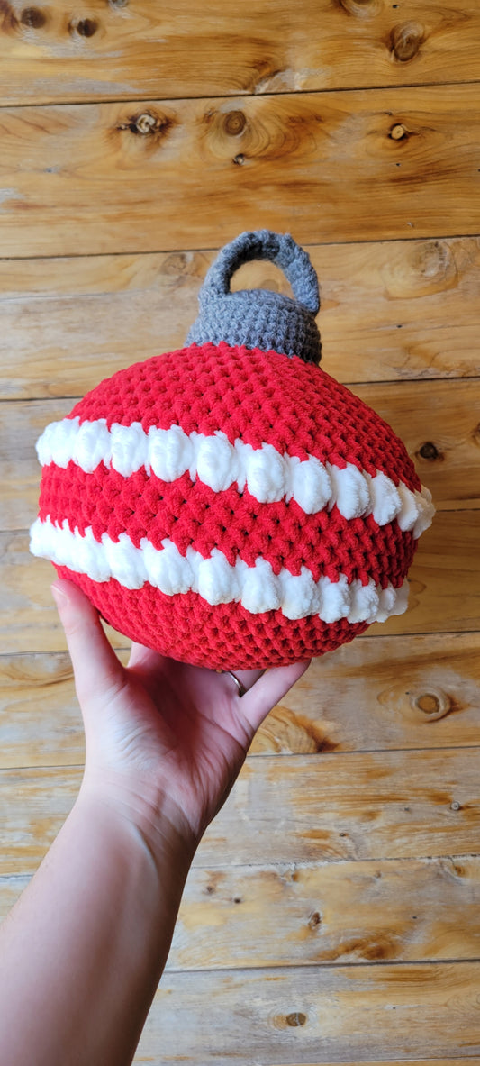 Hand holding a red and white striped ornament pillow with a gray handle against a wooden background