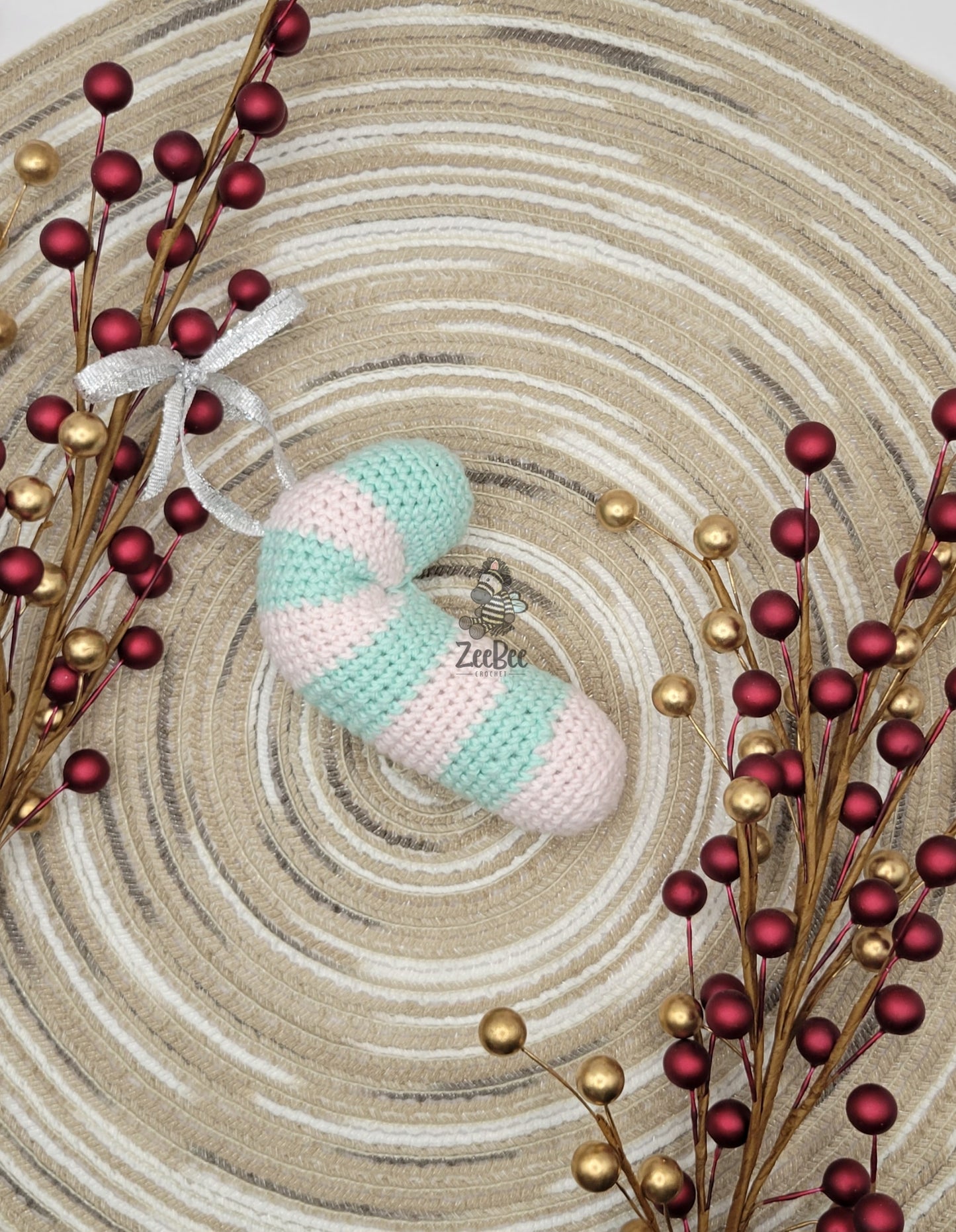 Crocheted candy cane ornament with striped pattern on a textured surface with decorative berries