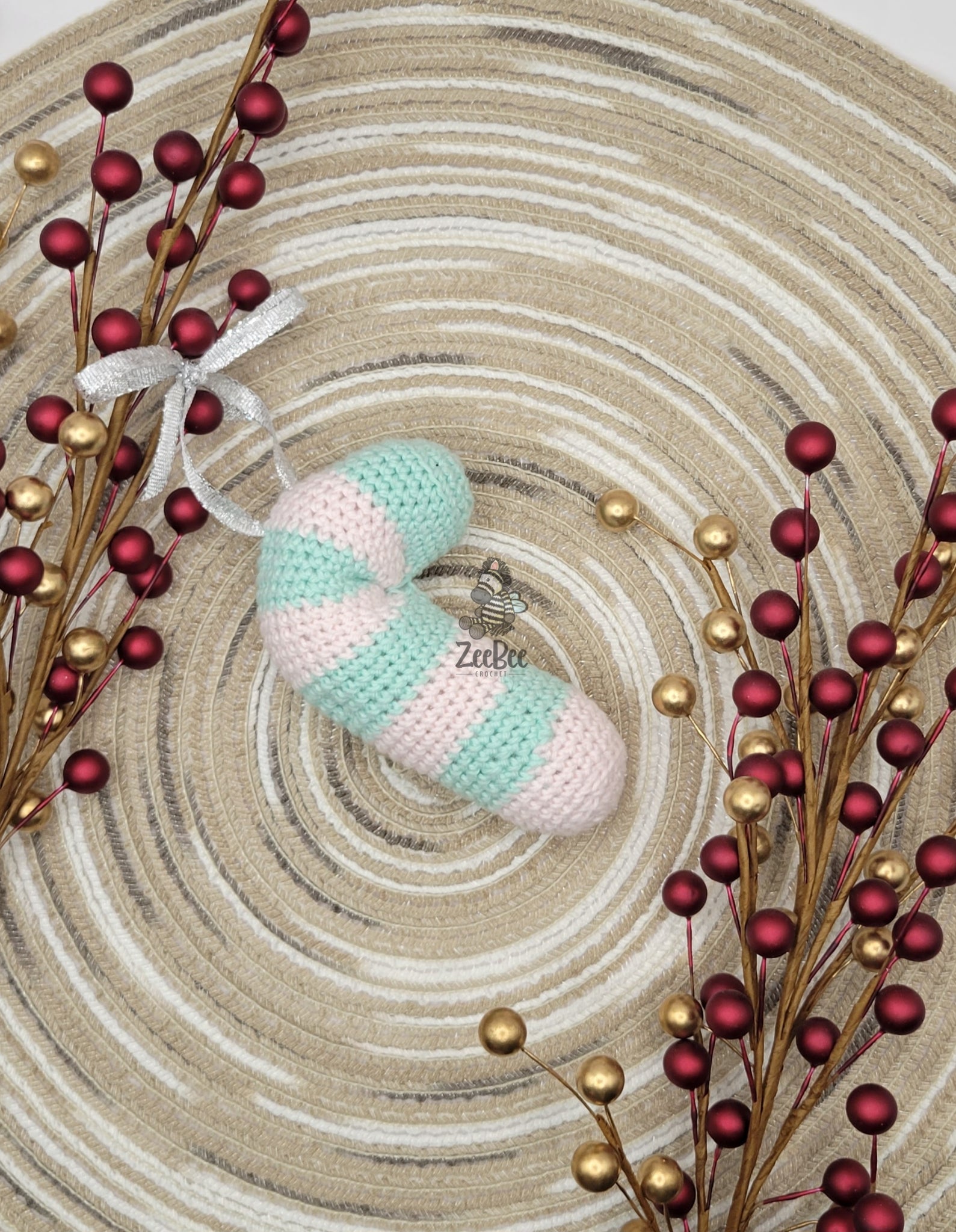 Crocheted candy cane ornament with striped pattern on a textured surface with decorative berries