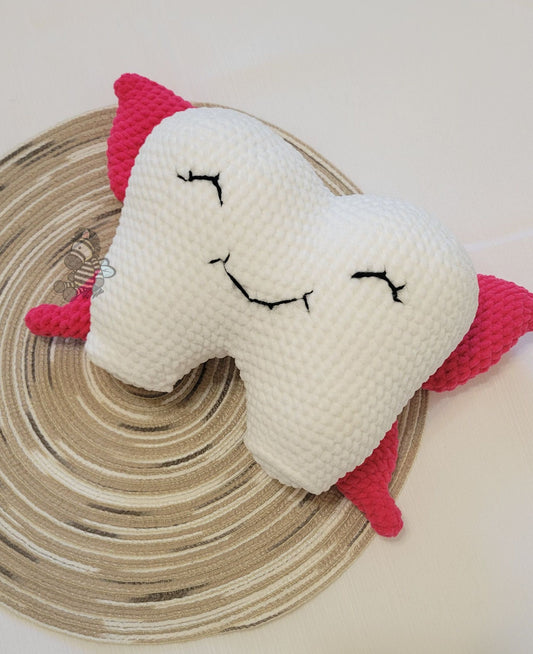 Pillow shaped like a tooth with closed eyes and a smile. It has pink wings. the background is a wood grain circle and white background.