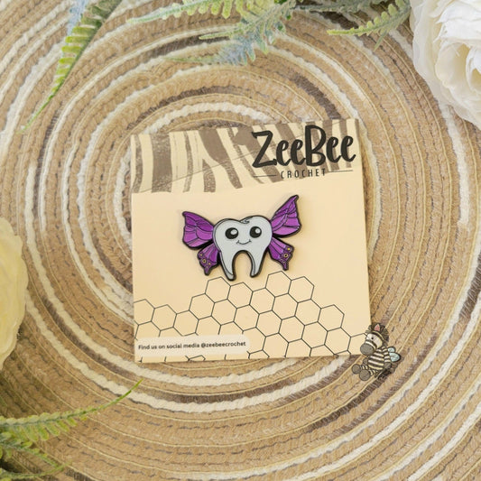 ZeeBee Crochet official tooth-fairy pin with purple wings on a wooden surface