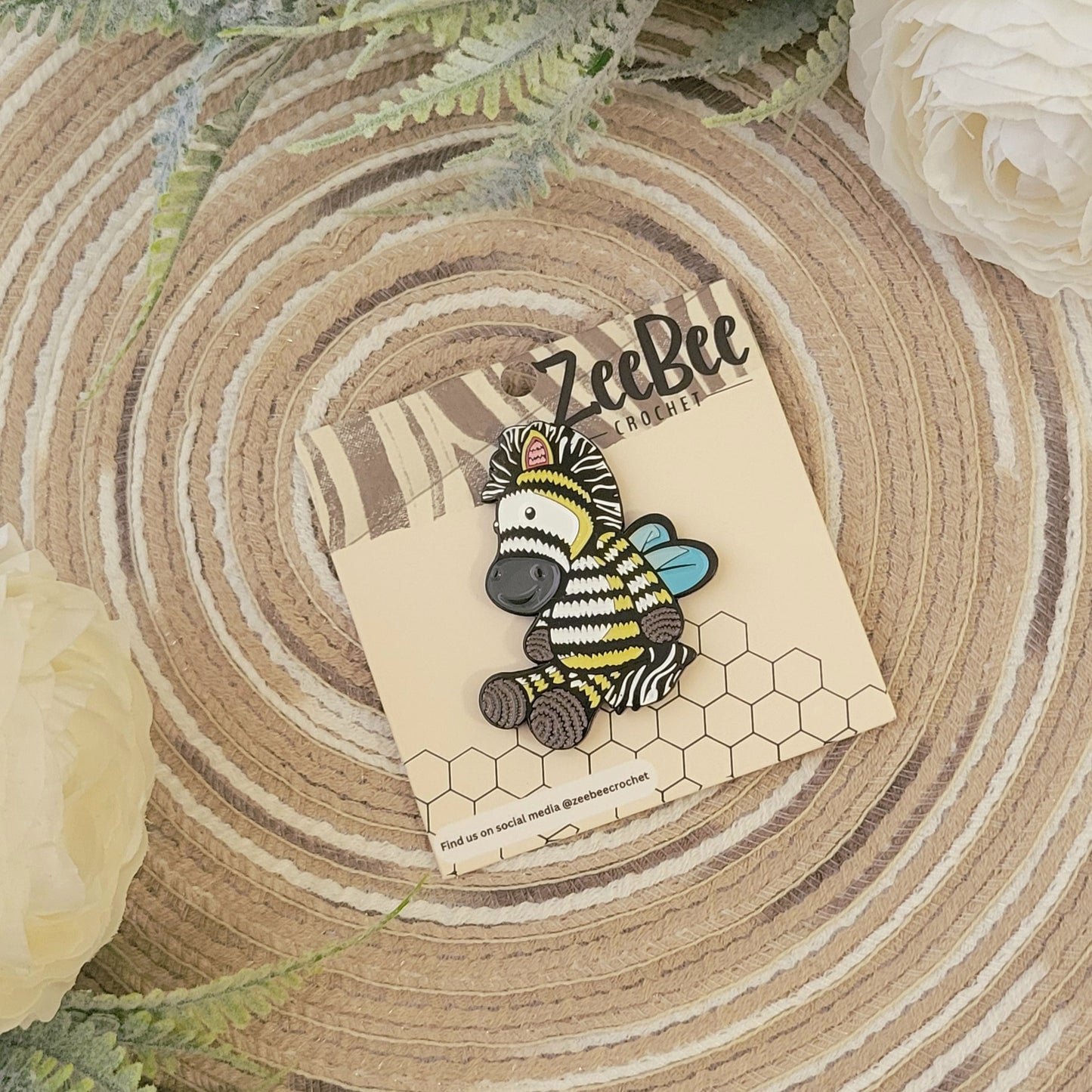 Zeebee pin on a card with 'ZeeBee' branding, placed on a wooden surface with flowers.