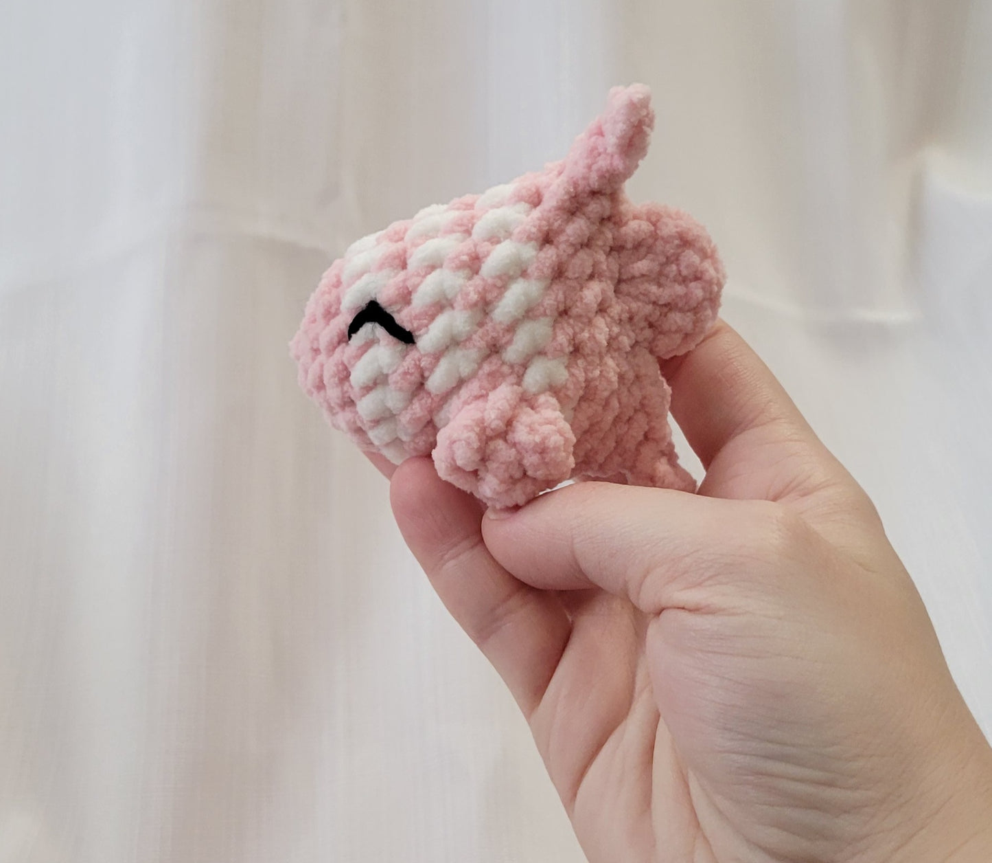 Hand holding a small pink and white crocheted fish toy against a plain white background